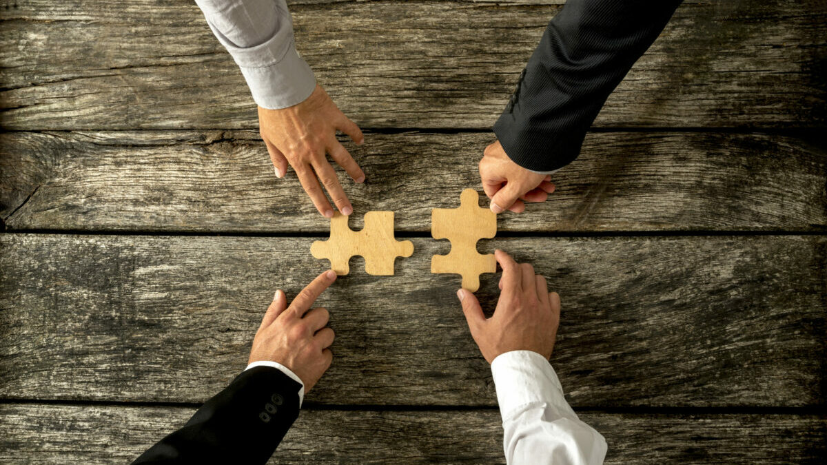 Hands placing puzzle pieces together symbolic of mergers and acquisitons